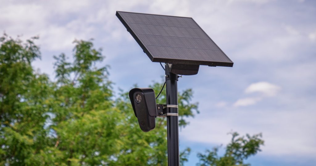 A Flock Safety automated license plate reader camera and solar panel mounted on a pole against a cloudy sky