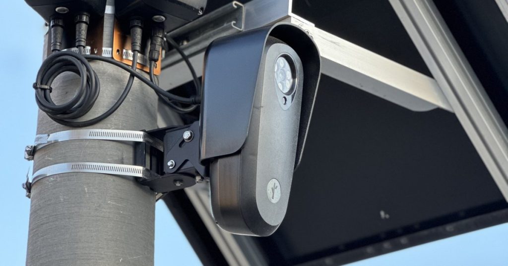 A Flock Safety license plate reader camera mounted on a street light pole beneath a solar panel