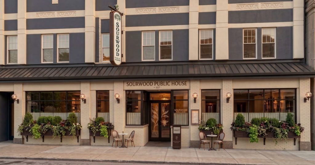 Rendering of a two-story brick building with a navy upper floor, a dark metal awning, a hanging Sourwood sign, window boxes and sidewalk tables